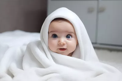 عکس کودک ناز زیر ملحفه ی سفید روی تخت
