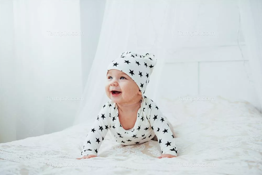 عکس نوزاد تازه متولد شده با لباس سفید و ستاره های سیاه روی تخت نرم و سفید در استودیو