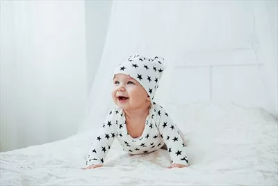 عکس نوزاد تازه متولد شده با لباس سفید و ستاره های سیاه روی تخت نرم و سفید در  استودیو