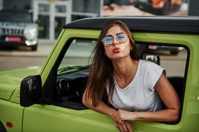 عکس زنی زیبا در خودروی مدرن سبز رنگ، در حال ژست گرفتن برای دوربین