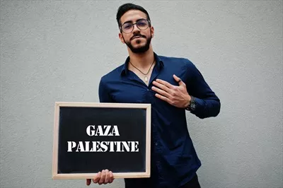 عکس مرد عرب با پیراهن آبی و عینک، تابلوئی با نوشته غزه و فلسطین در دست دارد