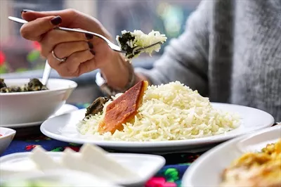 عکس تصویری از فردی که در حال خوردن غذا از بشقاب روی میز است