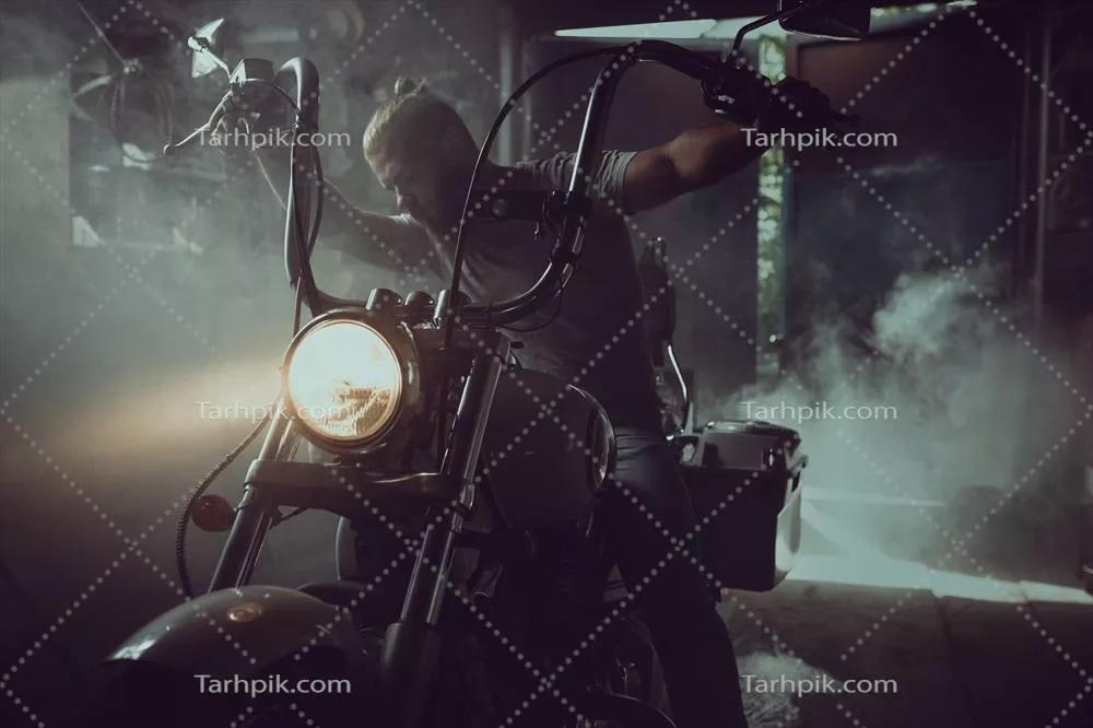 عکس مردی جذاب و خشن با ریش، نشسته بر روی موتورسیکلت در گاراژ خود