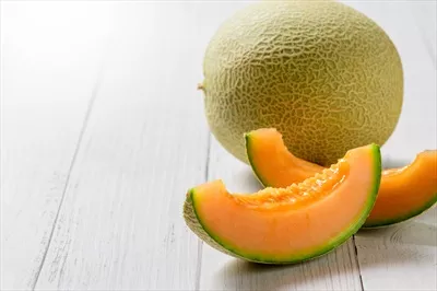 عکس برش های خوشمزه و تازه از ملون های ژاپنی بر روی میز چوبی سفید