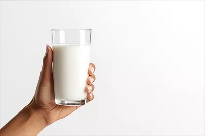 عکس دست گرفتن یک لیوان شیر تازه در پس زمینه خاکستری با فضای خالی