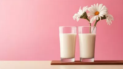 عکس دو لیوان شیر بر روی میز چوبی با گل و پس زمینه صورتی - نمادی از محصولات لبنی سالم