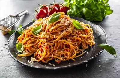 عکس پاستا اسپاگتی با سس گوجه فرنگی و بولونز، تزئین شده با پنیر پارمزان و ریحان