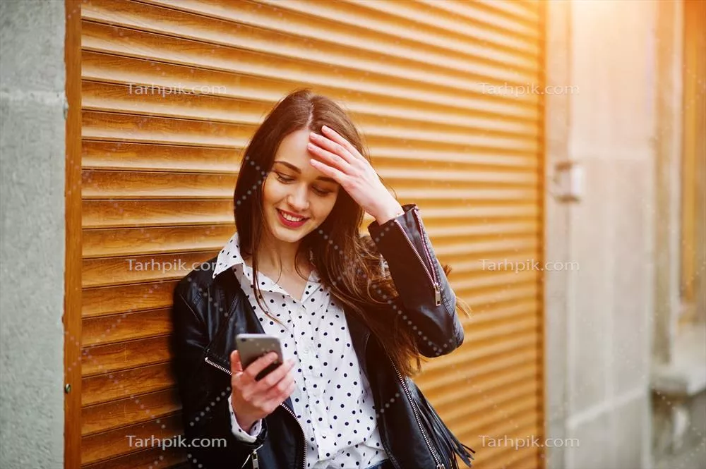 عکس پرتره ای از دختر جوان شیک با ژاکت چرم و گوشی موبایل در دست