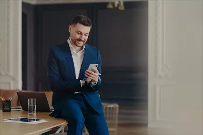 عکس مدیر خوشحال و خوش تیپ در حال بررسی موبایل خود در دفتر کار