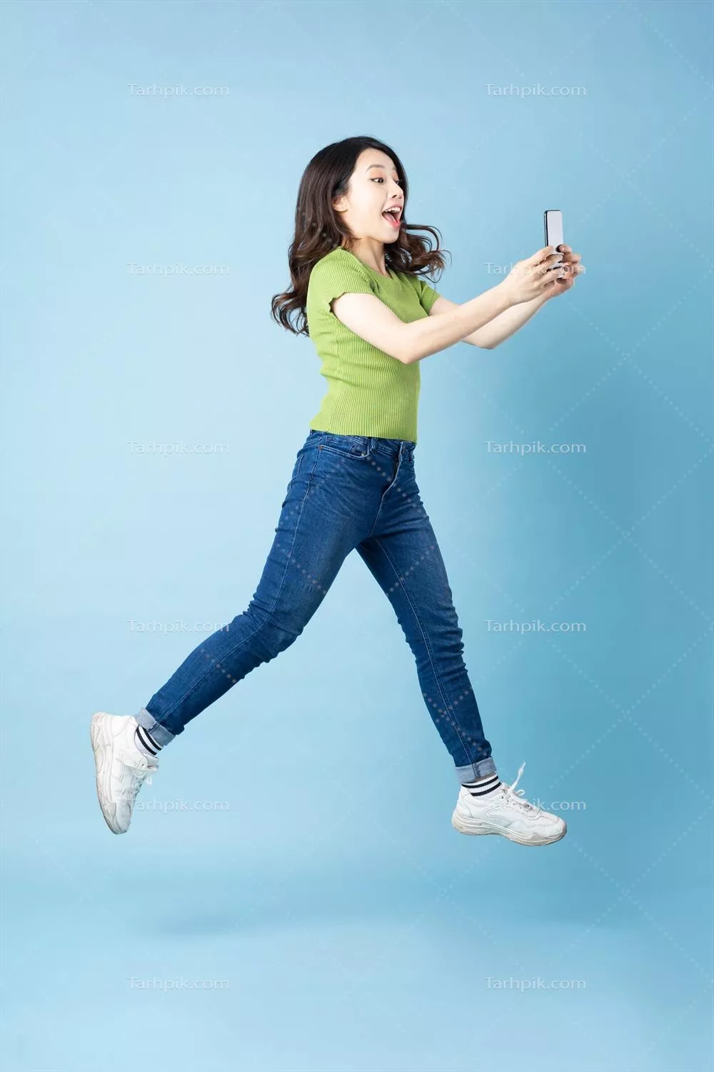 عکس پرتره ای از یک دختر جوان آسیایی زیبا که در حال پرش بر روی پس زمینه آبی است
