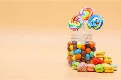 عکس مجموعه ای از شیرینی های متنوع در یک ظرف و ماکارون های فرانسوی بر روی زمینه ای کرم رنگ