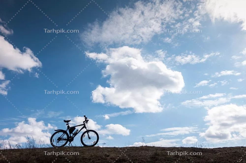 عکس سایه دوچرخه در آسمان آبی با ابرها، نماد استقلال و آزادی