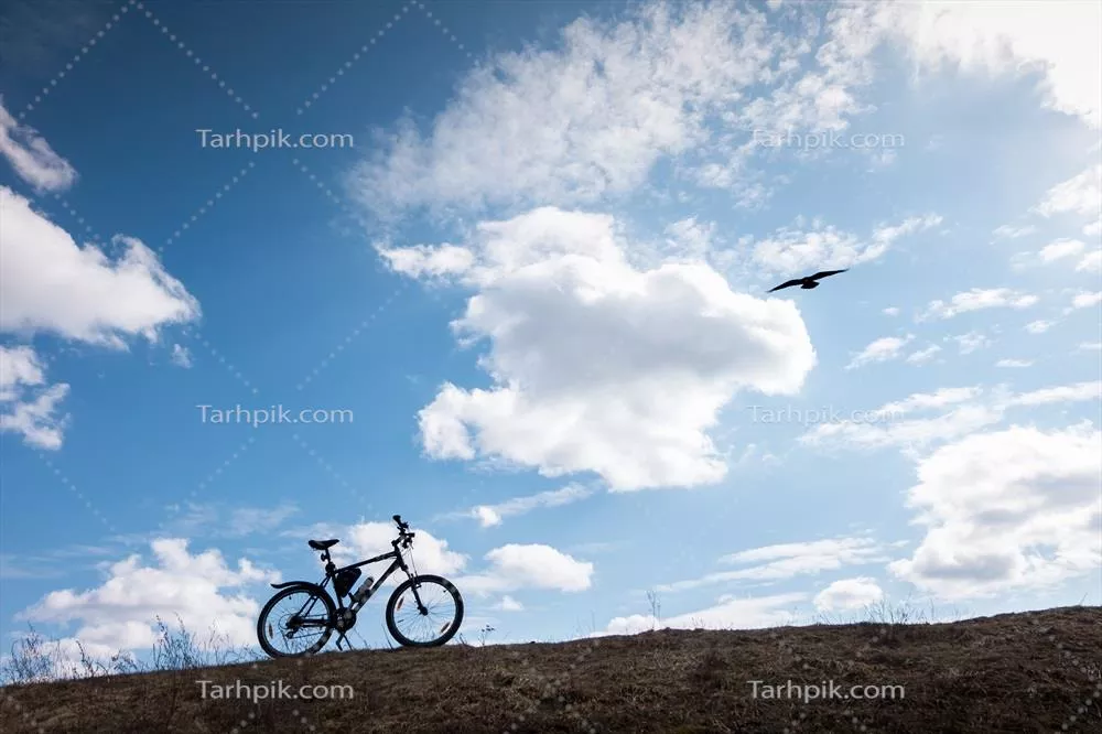 عکس سایه دوچرخه در آسمان آبی با ابرها، نماد استقلال و آزادی