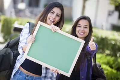 عکس دانش آموزان دختر با نژادهای مختلف در حال نشان دادن علامت تایید و نگه داشتن تخته سیاه خالی