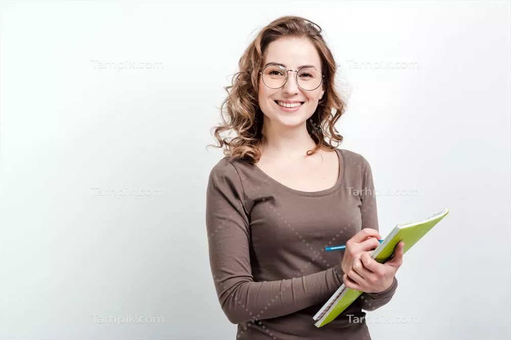 عکس دختر جذاب با عینک در حال یادداشت برداری در دفترچه ای سفید