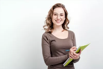 عکس دختر جذاب با عینک در حال یادداشت برداری در دفترچه ای سفید