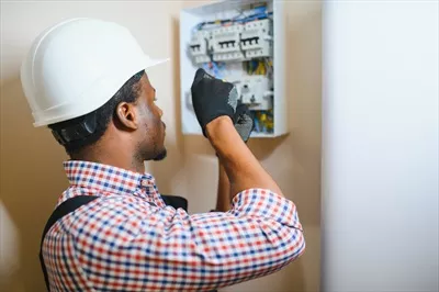 عکس برقکار مرد در حال کار بر روی تابلو برق و اتصالات الکتریکی