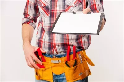 عکس نزدیک شدن به کارگر ماهر با کمربند ابزار و کلیپ بورد در پس زمینه خاکستری