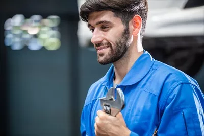 عکس مکانیک خوشحال و حرفه ای در حال بررسی خودرو در تعمیرگاه