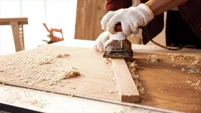 عکس نجار در حال استفاده از دستگاه پلانر برقی برای صاف کردن تخته در محل کار