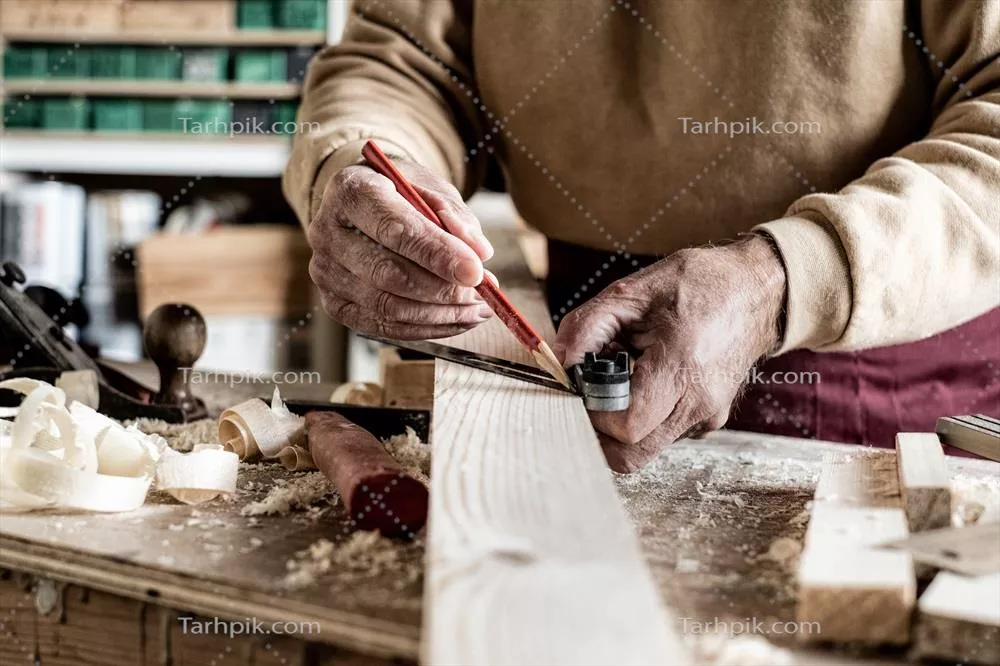 عکس نجار در حال اندازه گیری با مداد و خط کش فلزی بر روی تخته چوبی
