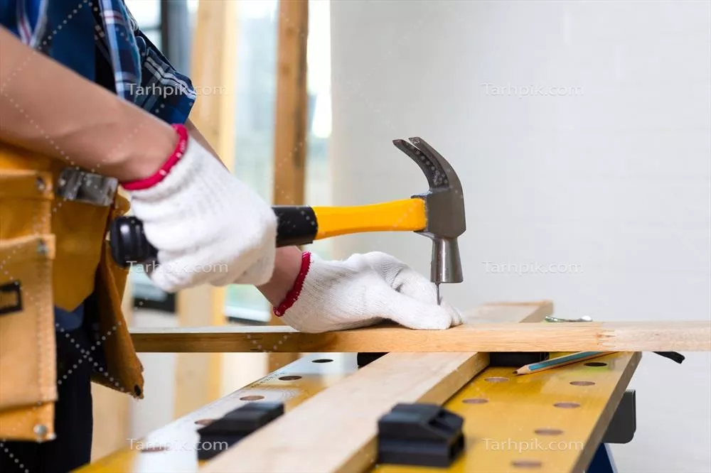 عکس کارگر ماهر در حال استفاده از چکش برای ساخت و ساز در کارگاه نجاری