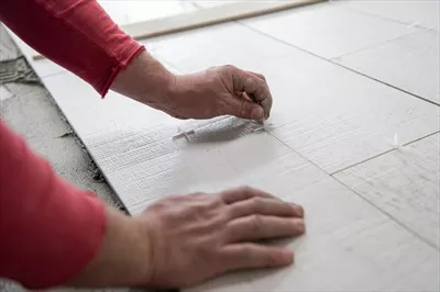 عکس نصب کاشی های سرامیکی با طرح چوب بر روی کف توسط کارگر ماهر