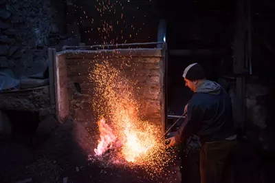 عکس کارگر جوان و سنتی آهنگری که با آتش باز کار می کند