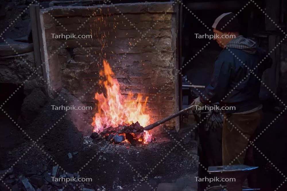 عکس کارگر جوان و سنتی آهنگری که با آتش باز کار می کند