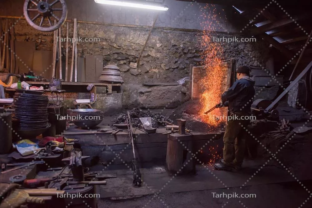 عکس کارگر جوان و سنتی آهنگری که با آتش باز کار می کند