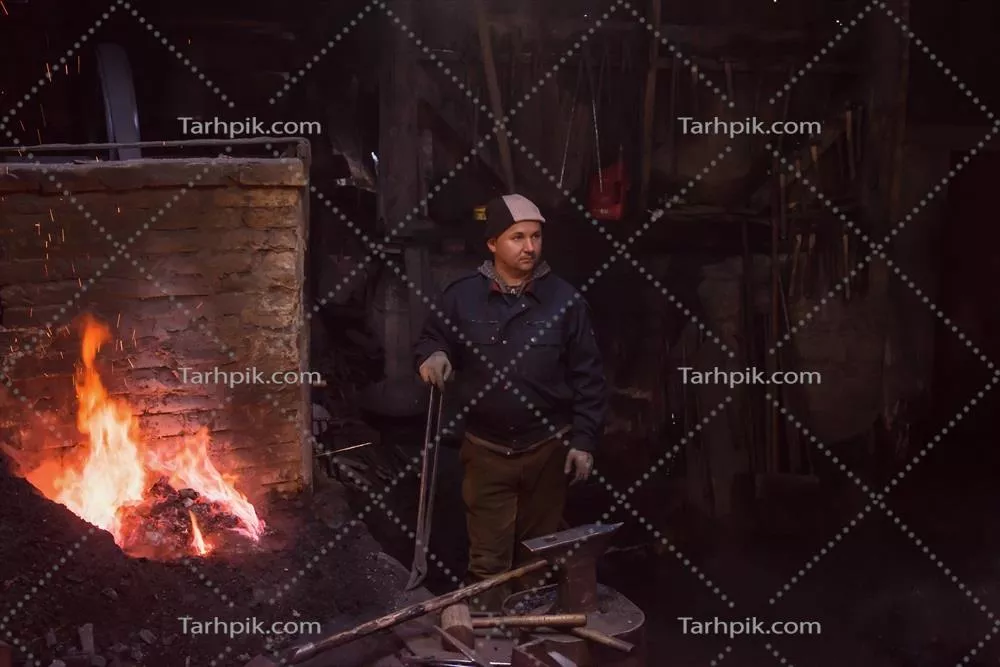 عکس کارگر جوان و سنتی آهنگری که با آتش باز کار می کند