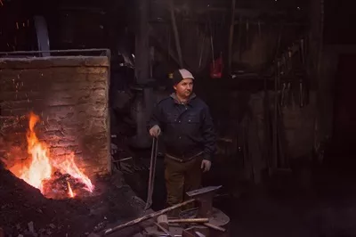 عکس کارگر جوان و سنتی آهنگری که با آتش باز کار می کند