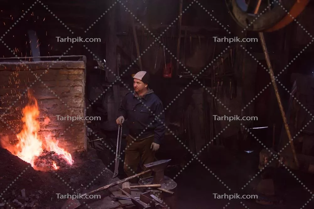 عکس کارگر جوان و سنتی آهنگری که با آتش باز کار می کند