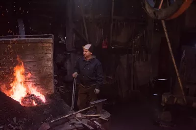 عکس کارگر جوان و سنتی آهنگری که با آتش باز کار می کند