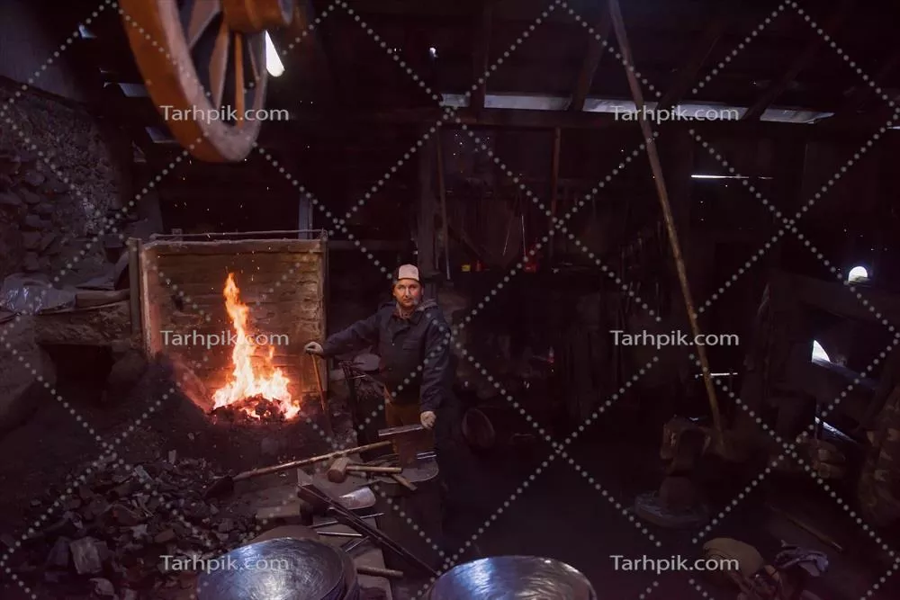 عکس کارگر جوان و سنتی آهنگری که با آتش باز کار می کند