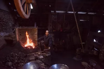 عکس کارگر جوان و سنتی آهنگری که با آتش باز کار می کند