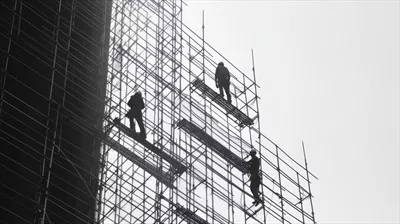 عکس کارگران ساختمانی در حال کار بر روی داربست در حین نوسازی ساختمان