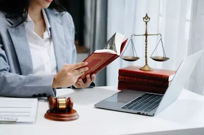 عکس زنی وکیل در حال مطالعه کتاب حقوقی با چکش قاضی در دفتر کار