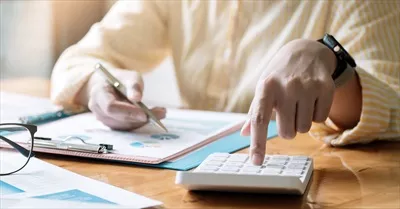 عکس حسابدار یا دفتردار در حال کار بر روی میز با استفاده از ماشین حساب