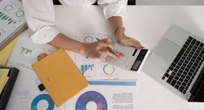 عکس زنی کارآفرین و حسابدار در حال استفاده از لپ تاپ و ماشین حساب برای مدیریت داده های مالی