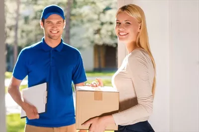 عکس خدمات تحویل سریع و باکیفیت: زن جوانی با جعبه کارتن و مرد تحویل دهنده خوشحال