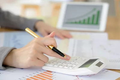 عکس دست یک زن با ماشین حساب و کاغذها در حال محاسبه مالیات