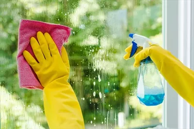 عکس زنی که در حال تمیز کردن شیشه با اسپری و دستمال است