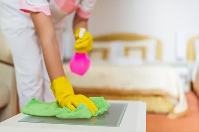 عکس نزدیک نمایی از خدمتکار هتل در حال تمیز کردن میز در اتاق