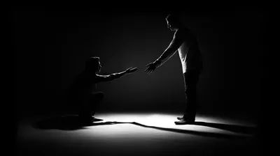 عکس تصویری از سیلوئت یک مرد در اتاق تاریک که به دیگری کمک می کند