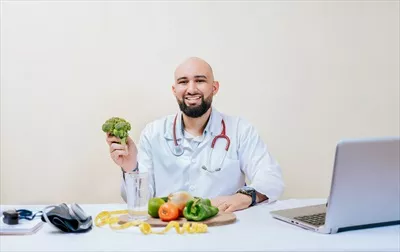 عکس تصویری از یک متخصص تغذیه خوشحال که بروکلی در دست دارد و در حال مشاوره است
