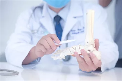 عکس پزشک ارتوپد در مطب خود در حال معاینه بیمار با مدل پا