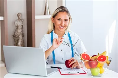 عکس مشاوره تغذیه با لبخند: متخصص تغذیه در دفتر کارش با سبزیجات و میوه های سالم