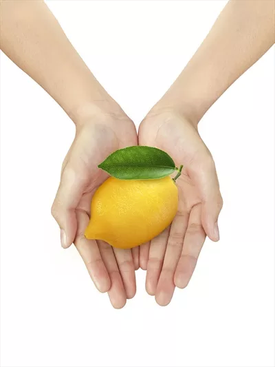 عکس زنی زیبا با دستش لیمو زرد را در پس زمینه ای سفید نگه داشته است