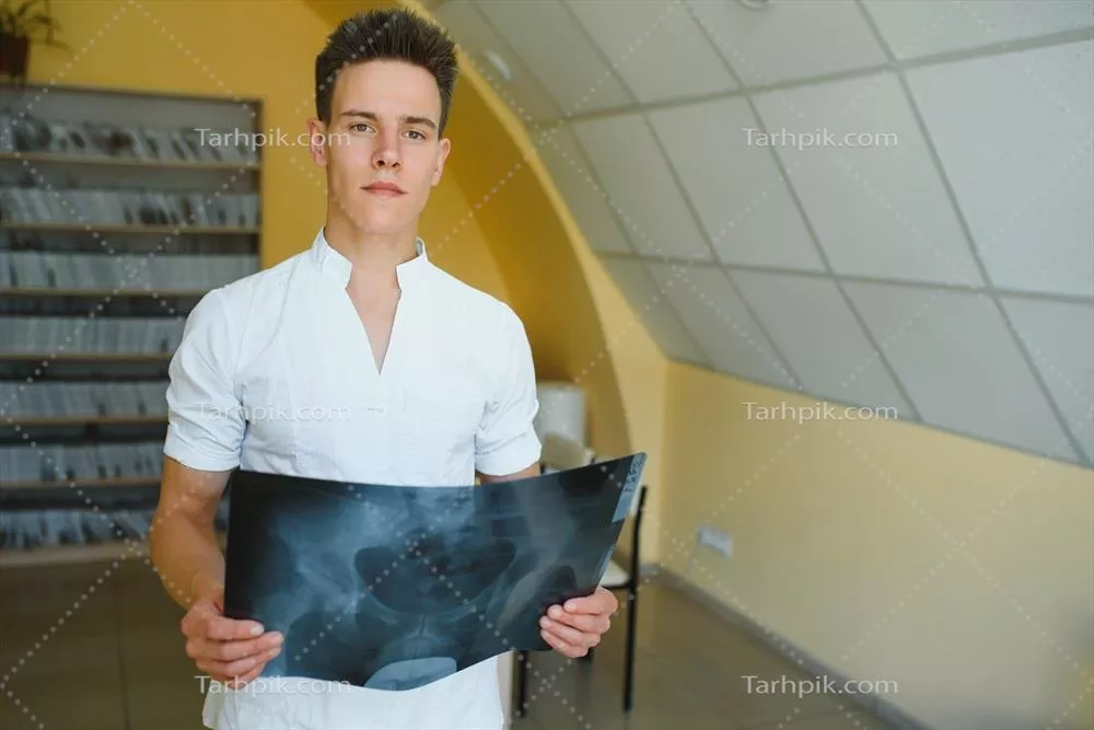 پزشک جذاب در حال بررسی عکس رادیولوژی و لبخند زدن به دوربین